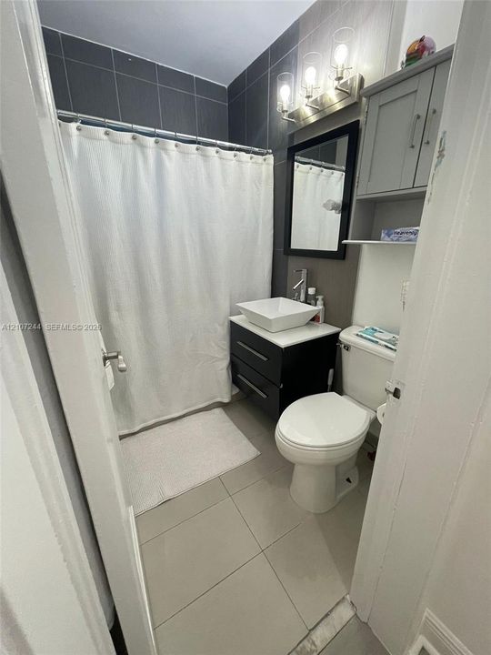 Bathroom featuring a vanity with a square vessel sink, dark-toned wall-mounted cabinetry, a three-light fixture, and large-format wall tiling in the shower area