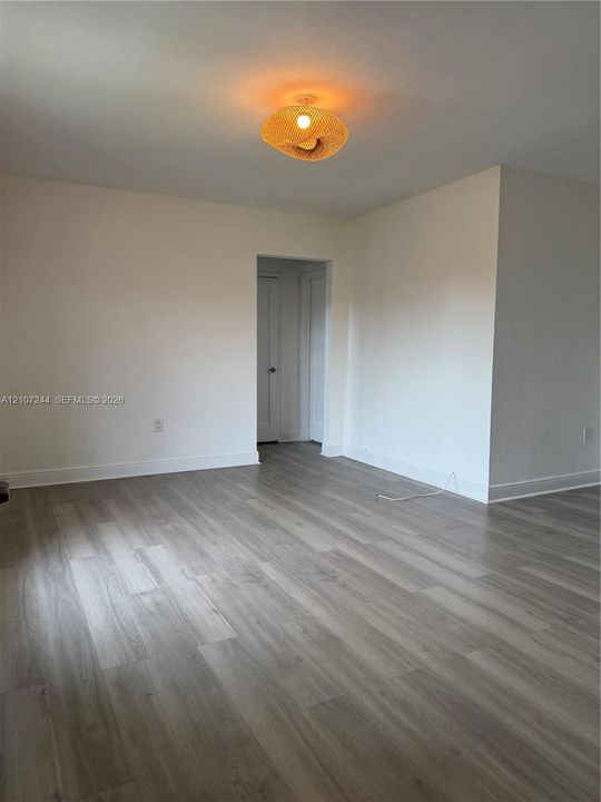 Interior space featuring wood-finish flooring, smooth white walls, and a woven basket-style ceiling light fixture