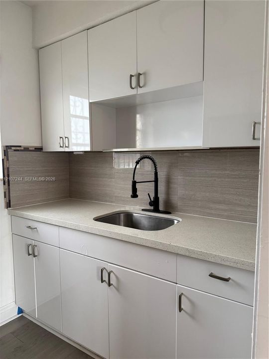 Kitchen featuring gloss-finish cabinetry, stone-texture countertops, a stainless steel undermount sink, a matte black high-arch faucet, and a horizontal-tile backsplash