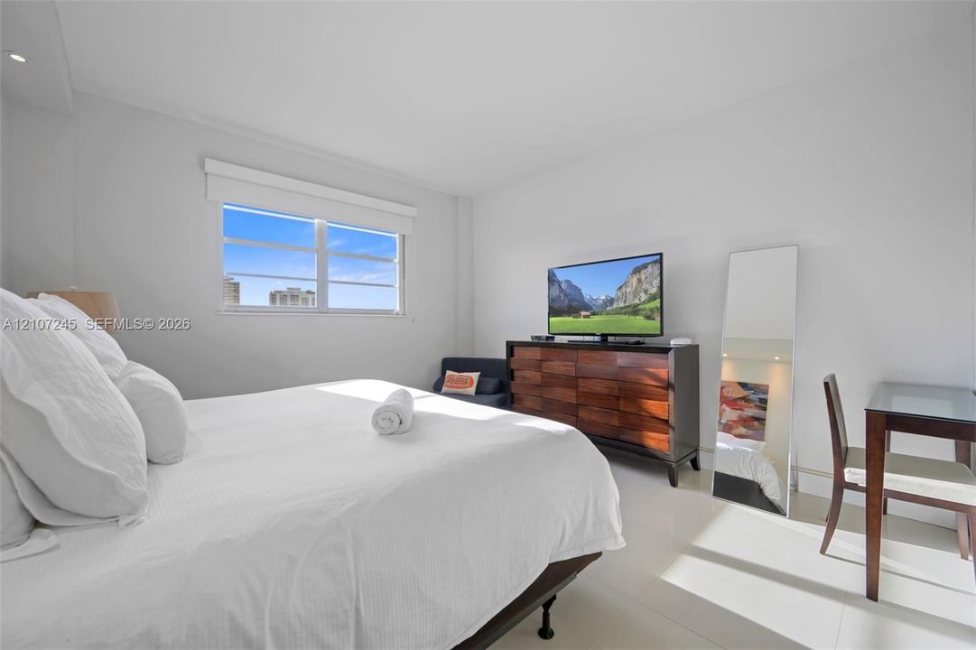 Neutral-toned bedroom featuring white-finish tile flooring, recessed ceiling lighting, and a window with a horizontal blind