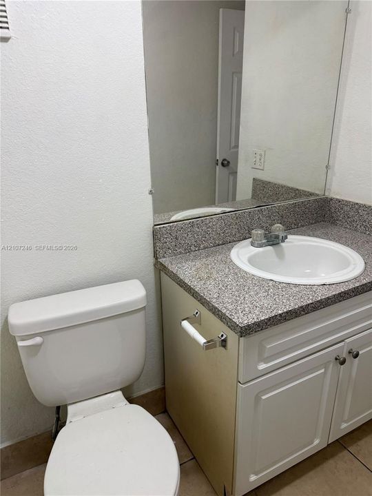 Bathroom vanity featuring white cabinetry, a neutral-toned stone-finish countertop, an integrated drop-in sink, and a large-format frameless mirror