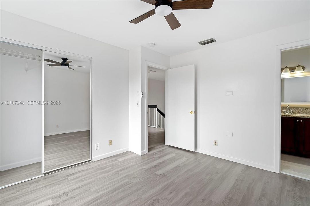 Room featuring wood-finish flooring, a mirrored sliding-door closet, and a ceiling-mounted fan with integrated lighting