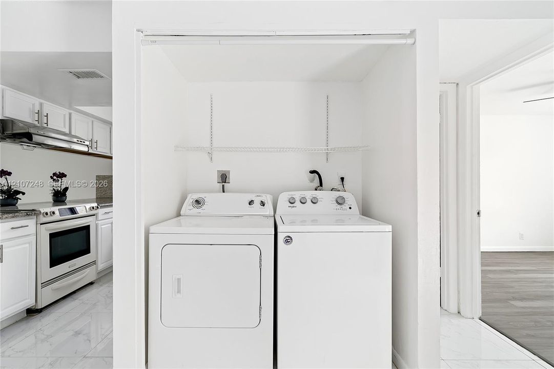 Laundry alcove featuring white-finished cabinetry, adjustable metal shelving, and white tile flooring