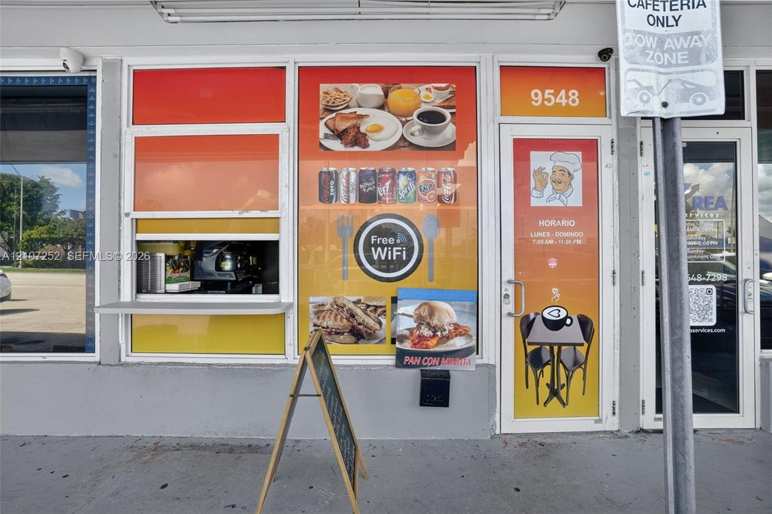 Commercial storefront featuring aluminum-framed glass windows, a service pass-through window with an exterior counter, and a glass-paneled entry door
