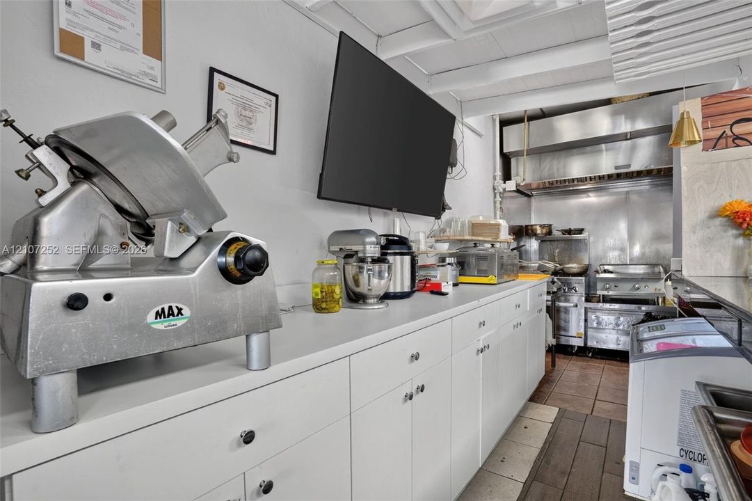 Commercial kitchen space featuring stainless steel prep surfaces, white cabinetry with integrated hardware, professional-grade metal ventilation hood, and tile flooring