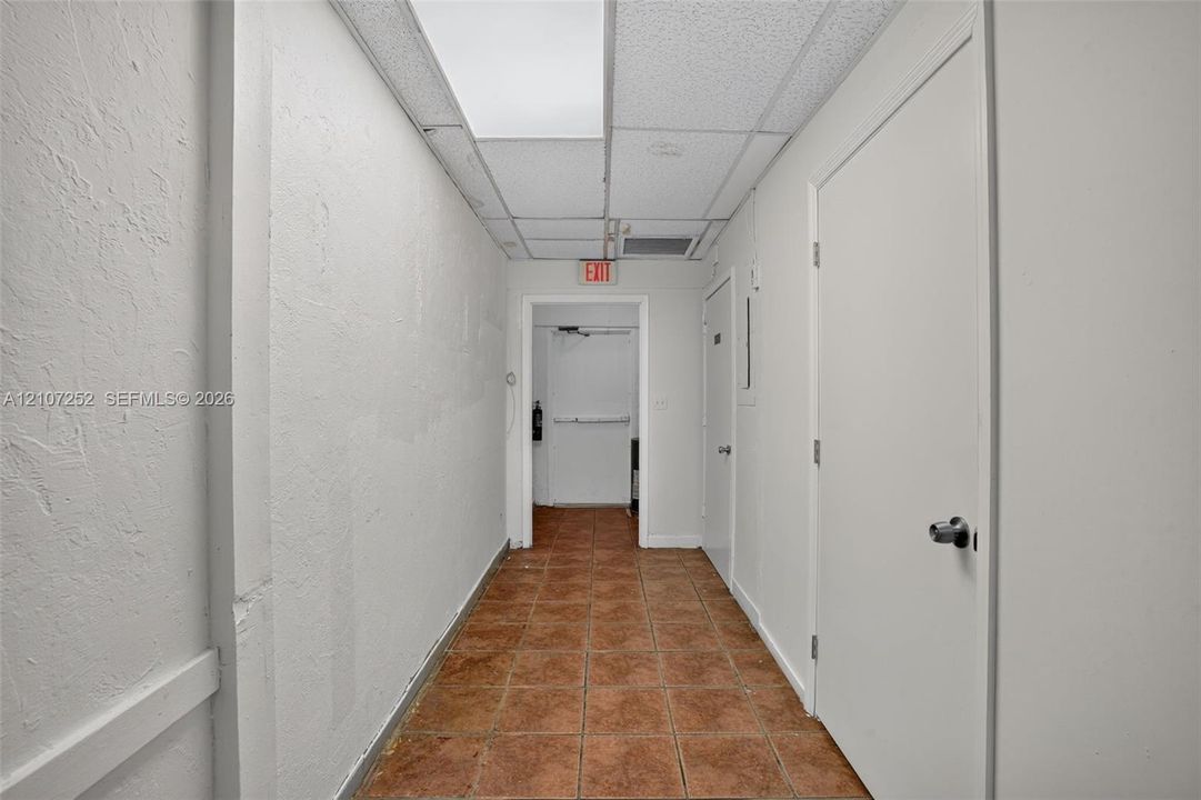 Interior corridor featuring ceramic tile flooring, textured wall finishes, and a drop ceiling with recessed lighting
