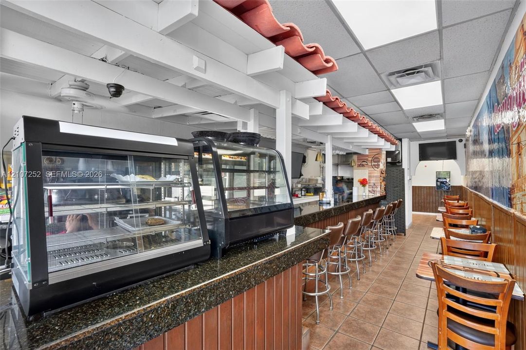 Commercial kitchen area featuring a dark stone-finish service counter, red decorative roof tiles, wood-paneled wainscoting, and tile flooring