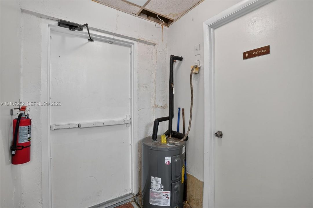 Utility area featuring a steel exit door with push-bar hardware, a water heater, a wall-mounted fire extinguisher, and a panel door with signage