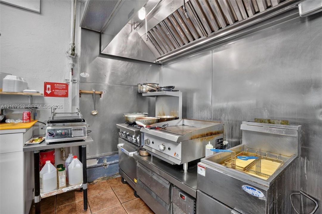 Commercial kitchen featuring a stainless-steel hood ventilation system, stainless-steel wall paneling, a professional-grade griddle, a deep fryer, and a multi-burner gas range