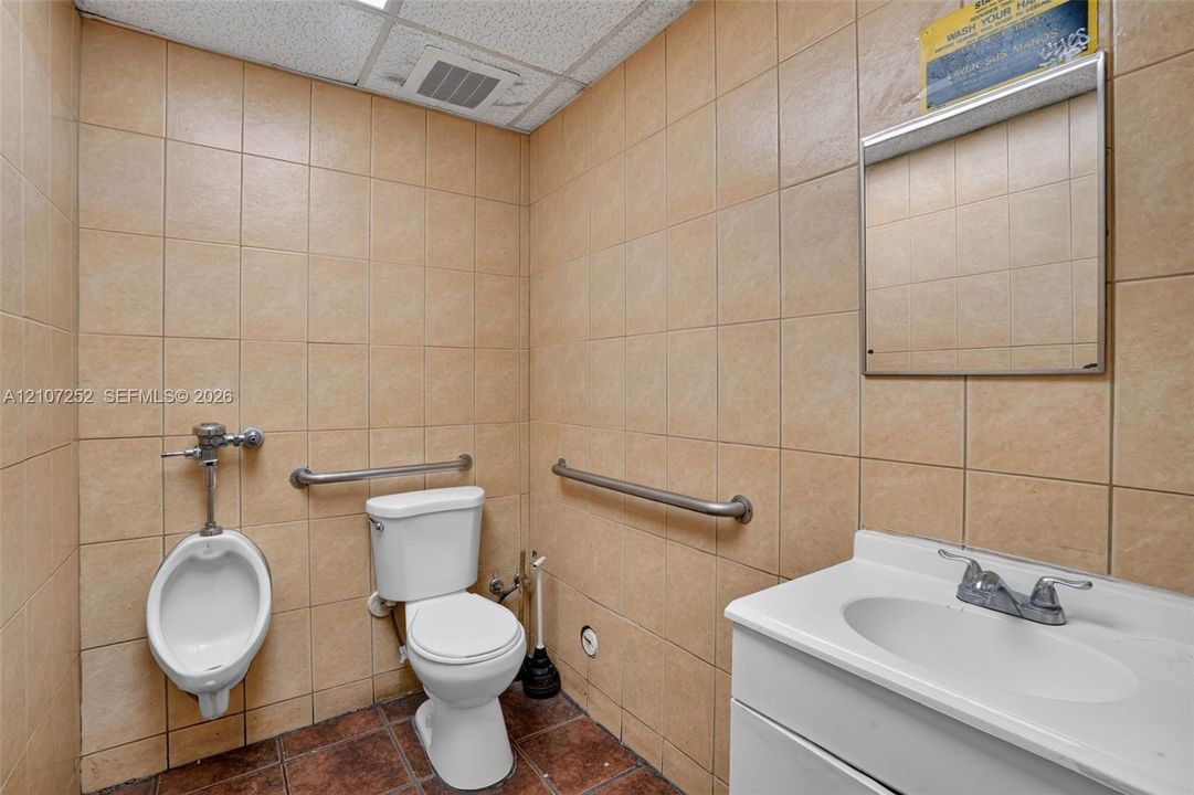 Restroom featuring floor-to-ceiling ceramic wall tiling, pedestal sink with chrome dual-handle faucet, wall-mounted mirror, and stainless steel grab bars