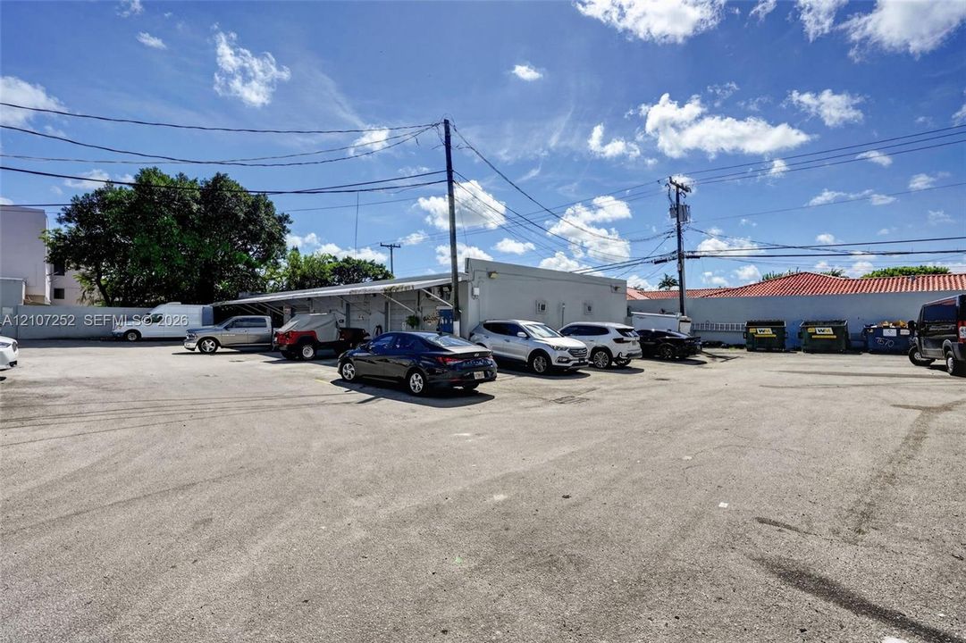 Extensive asphalt parking area featuring a concrete structure with covered exterior bays and a perimeter wall