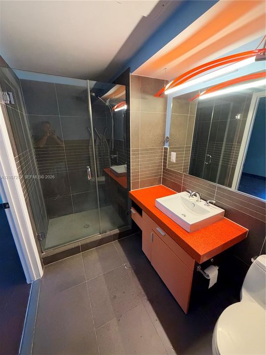 Bathroom featuring a glass-enclosed shower, wall-mounted vanity with a rectangular vessel sink, large-format tile flooring, and integrated wall lighting