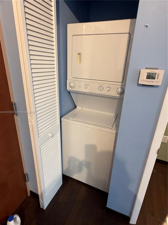 Stackable laundry unit with white finish, louvered bi-fold closet door, and digital wall-mounted thermostat