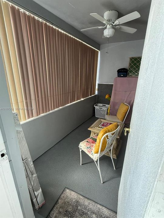 Enclosed space featuring expansive windows with vertical blinds, a ceiling-mounted fan, and solid flooring