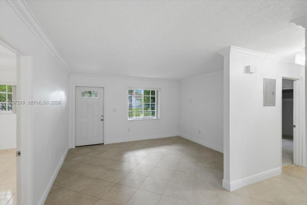 Neutral interior featuring large-format ceramic tile flooring, crown molding, a multi-pane window, and an exterior door with integrated glass paneling