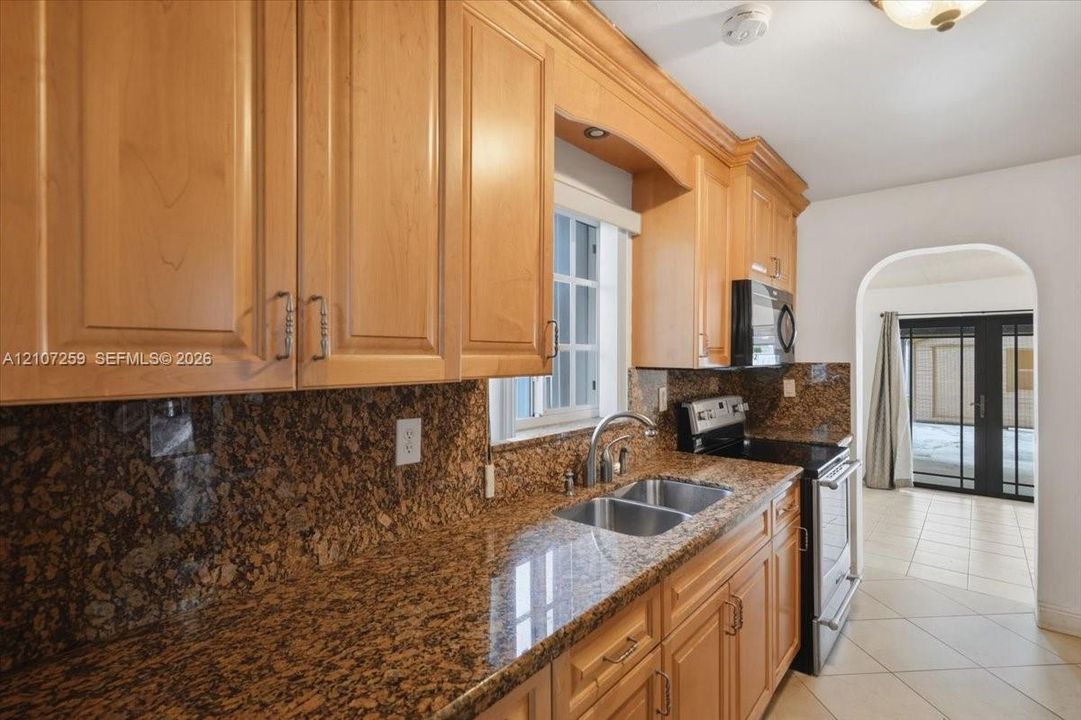 Kitchen featuring natural wood cabinetry, stone countertops, dual-basin stainless steel sink with pull-down faucet, and black built-in microwave range