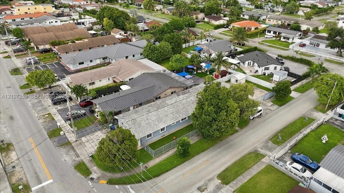 Aerial perspective of a single-story residence featuring a shingle roof, exterior wall cladding, and a fenced yard with mature trees
