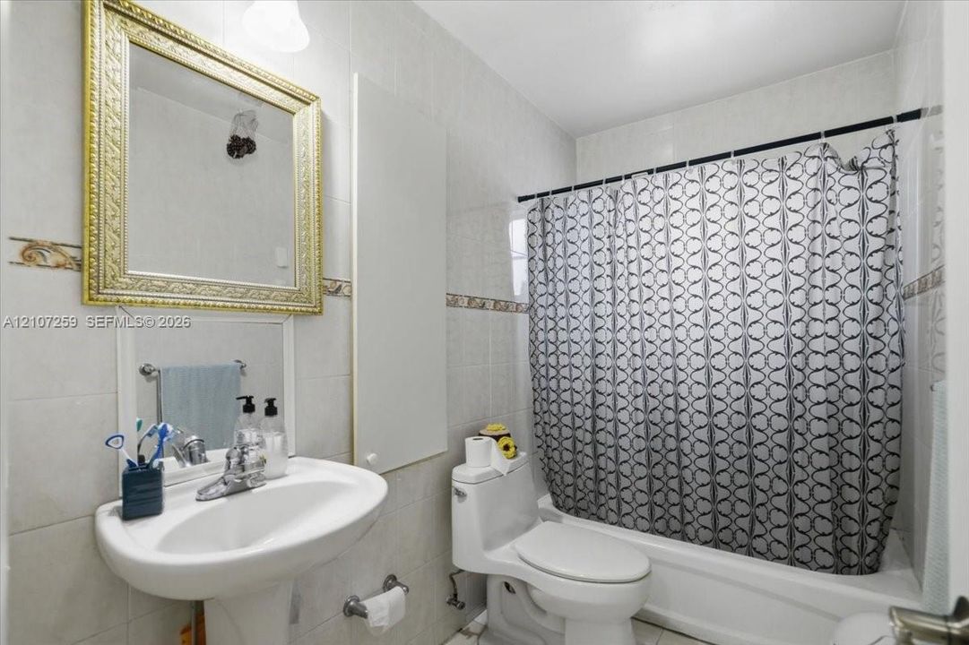 Full-wall ceramic tile surround, pedestal sink with polished chrome faucet, and integrated tub-shower combination