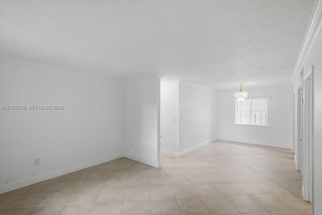 Neutral-toned ceramic tile flooring, crown molding, and a suspended multi-tier chandelier in a bright interior space