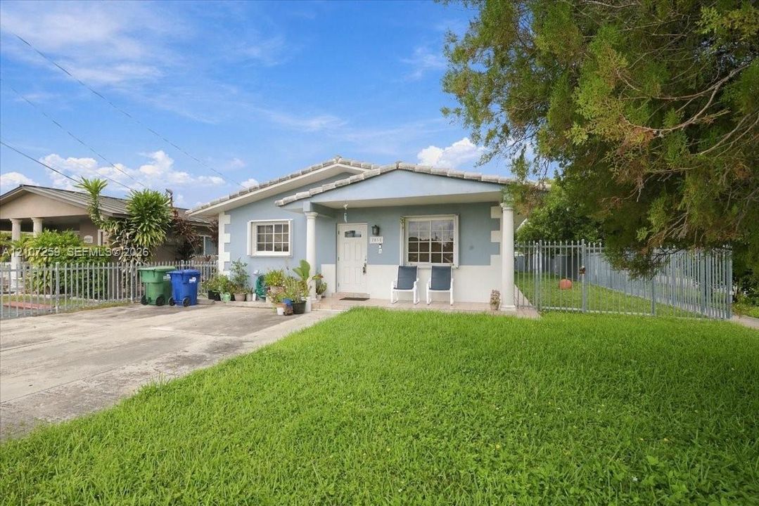 Single-story exterior featuring a covered front porch with decorative columns, a concrete driveway, and metal perimeter fencing