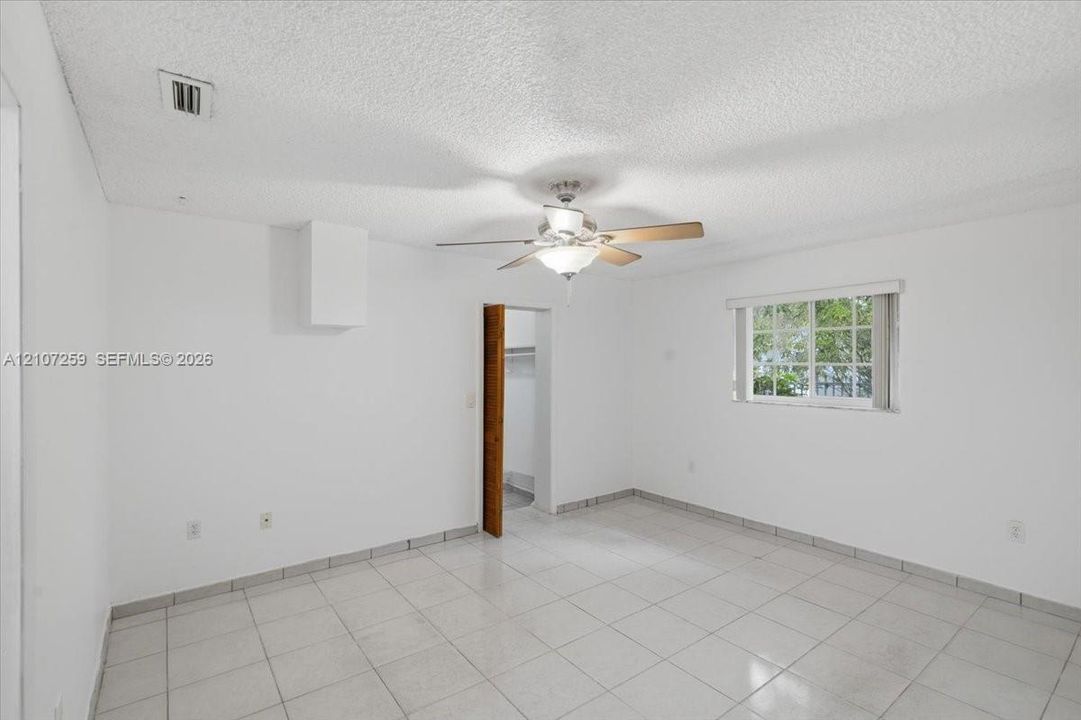 Interior space featuring white-painted walls, light-toned ceramic tile flooring, a central ceiling fan with integrated lighting, and a window with white casing