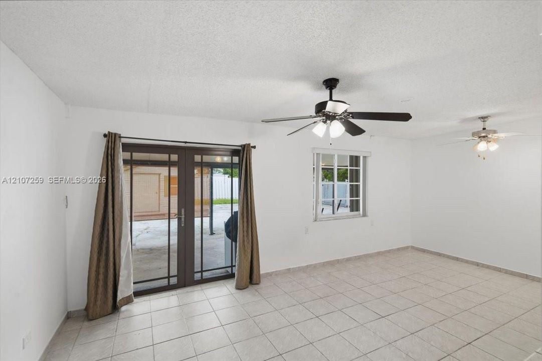 Interior space featuring white walls, tile flooring, two ceiling fans with integrated lighting, and glass French doors