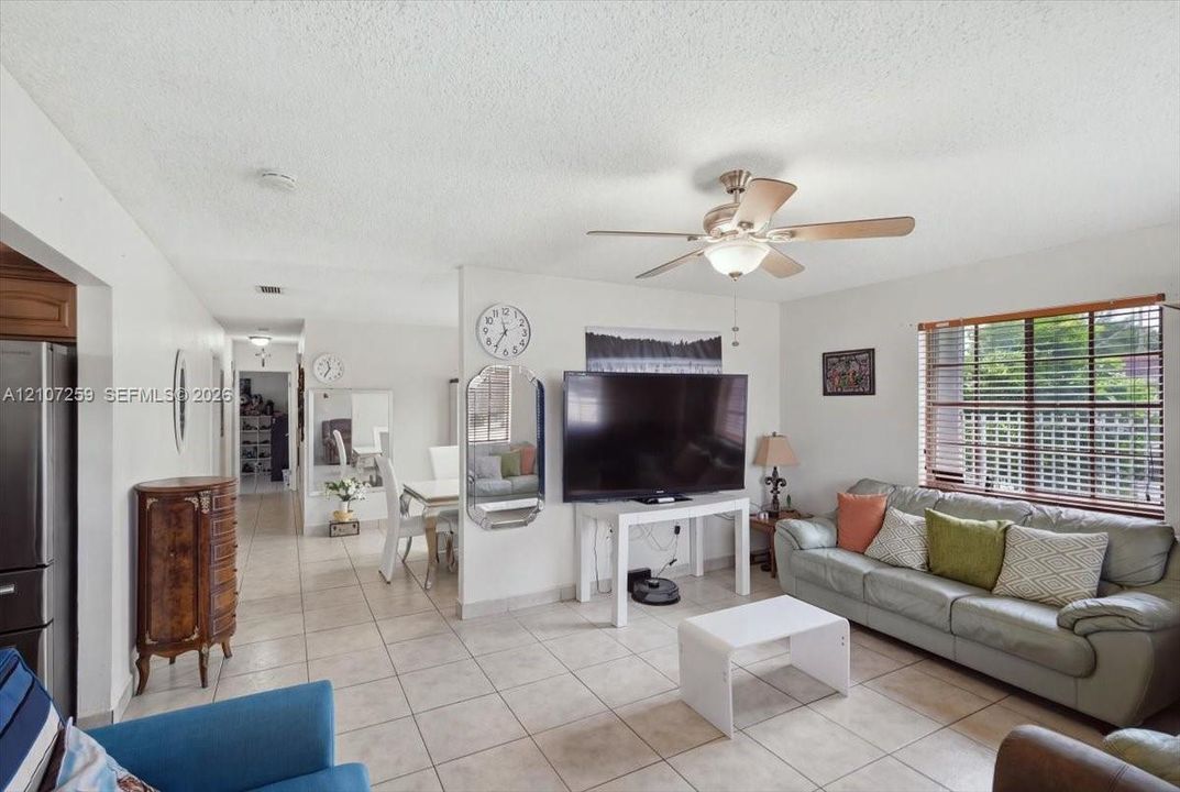 Neutral tile flooring, ceiling-mounted light fixture with fan, and window featuring horizontal blinds