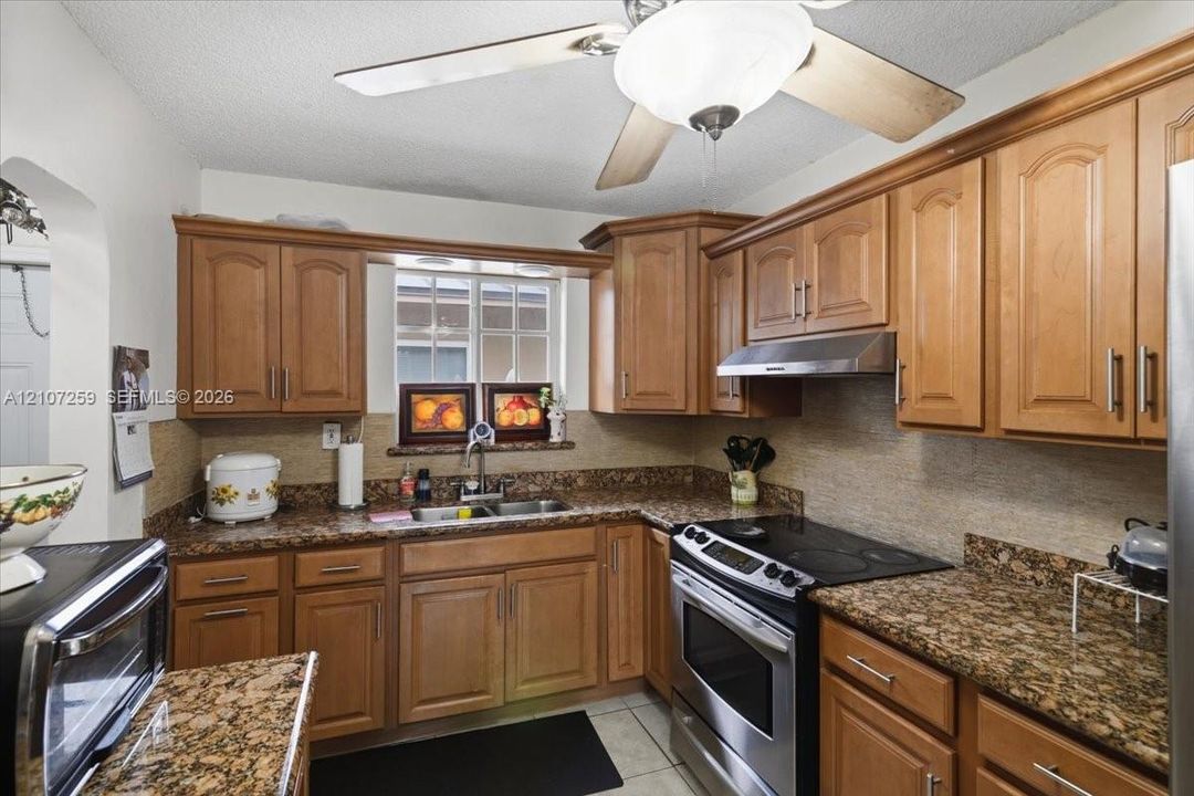 Kitchen featuring natural wood cabinetry, stone-patterned countertops, a stainless steel range, a coordinating range hood, and a dual-basin undermount sink