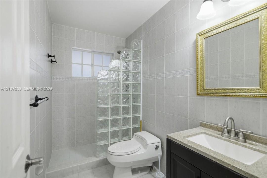 Full-wall ceramic tile, glass block shower enclosure, stone-finish vanity countertop, under-mount sink, and dark wood-finish cabinetry