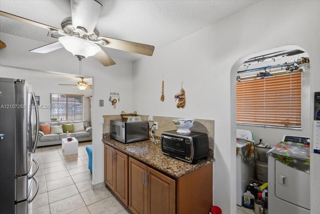 Kitchen featuring wood cabinetry, stone-finish countertops, ceramic tile flooring, and a ceiling fan with integrated lighting