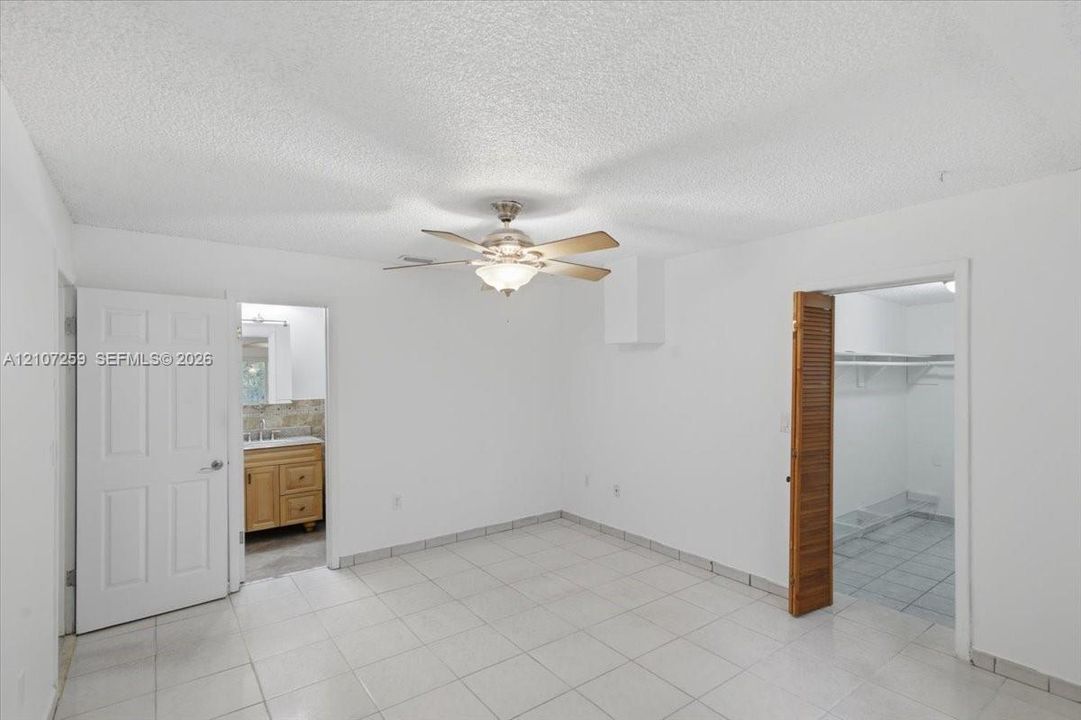 Interior space featuring ceramic tile flooring, a centered ceiling fan with integrated lighting, a wooden louvered closet door, and a solid-core six-panel door