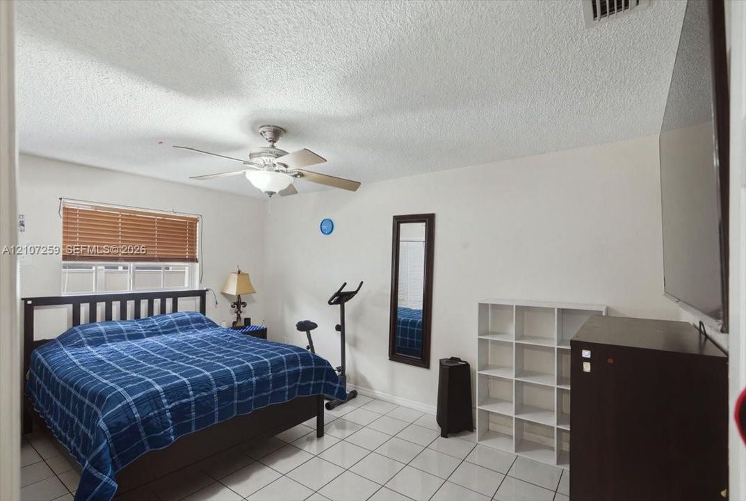 Neutral-toned interior featuring ceramic tile flooring, a ceiling-mounted light fixture with fan blades, and a window finished with horizontal blinds
