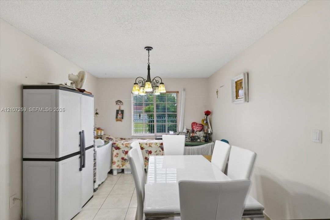 Ceramic tile flooring, multi-light hanging chandelier, and large window with security bars