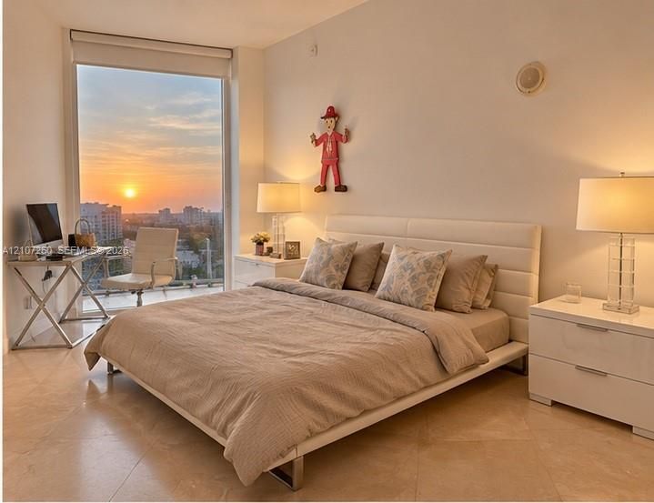 Floor-to-ceiling window featuring a sunset backdrop, polished tile flooring, and integrated ceiling speaker