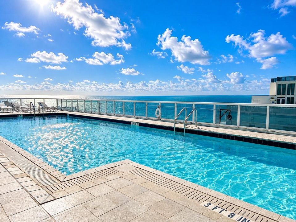 Elevated swimming pool featuring stone-tile decking, metal safety railing, and integrated pool drainage
