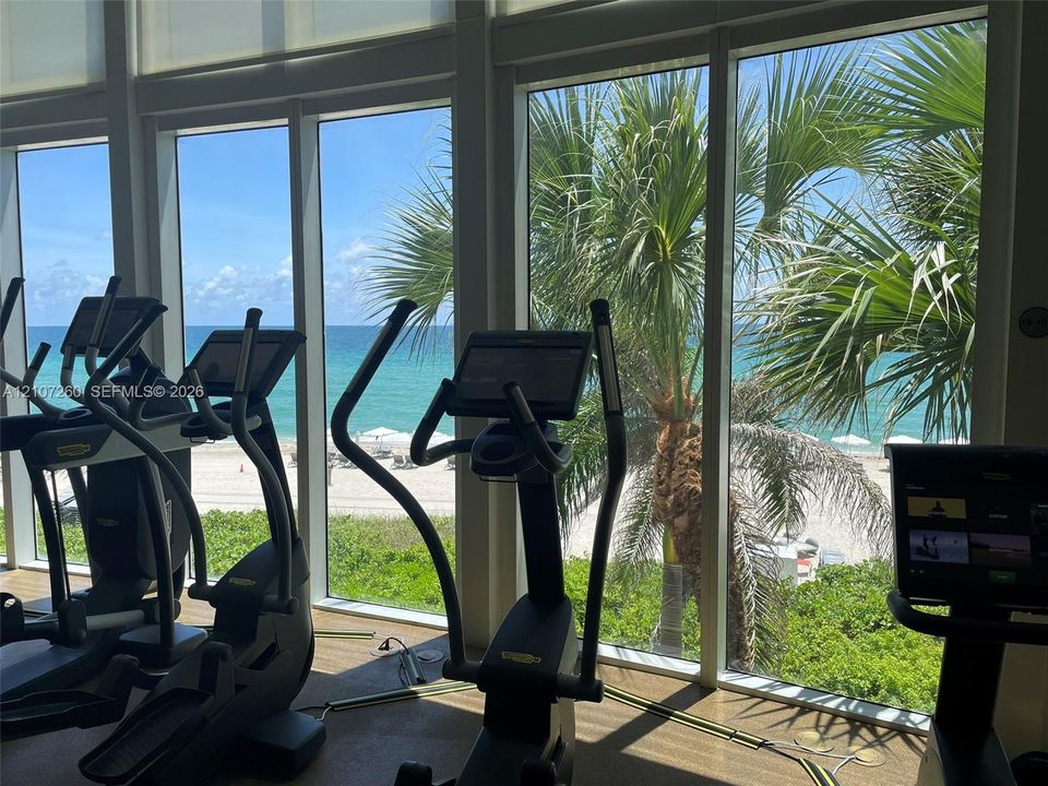 Floor-to-ceiling windows featuring ocean and beach scenery, integrated roller shades, and textured flooring