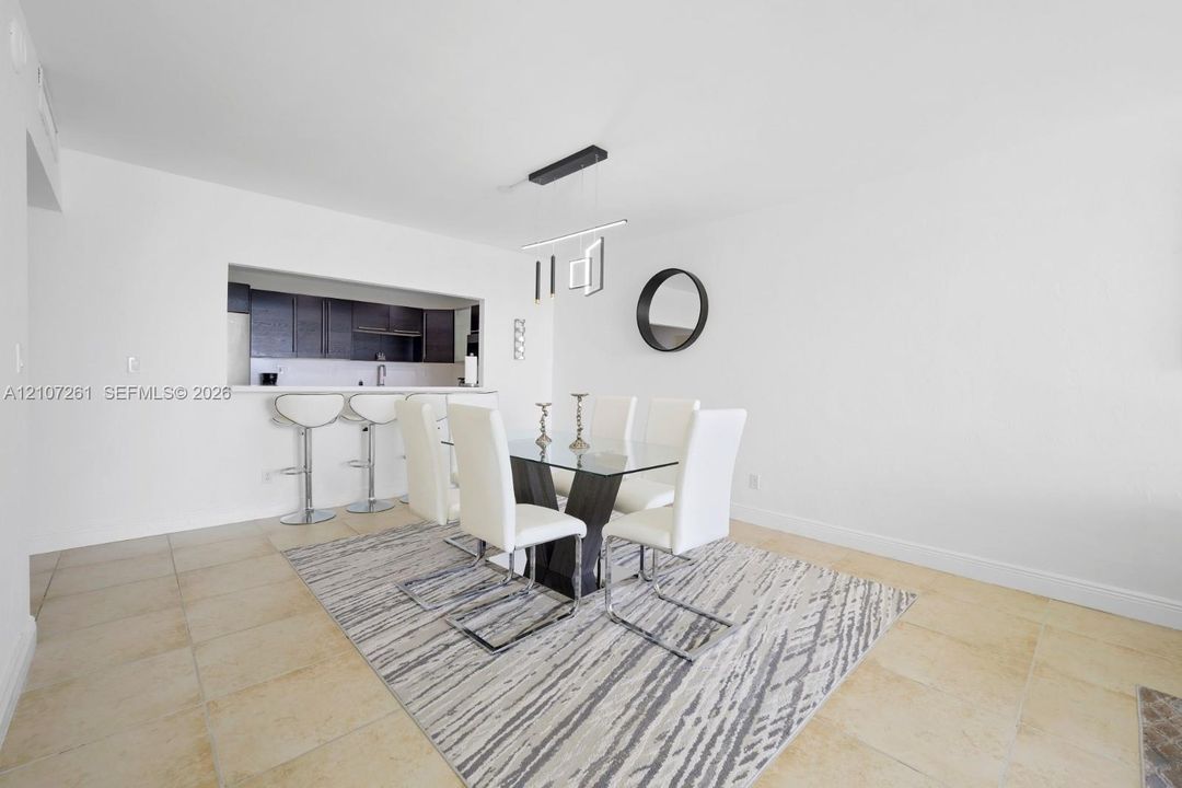 Dining area featuring large-format tile flooring, a pass-through opening to the kitchen, a breakfast bar, and a modern linear pendant light fixture
