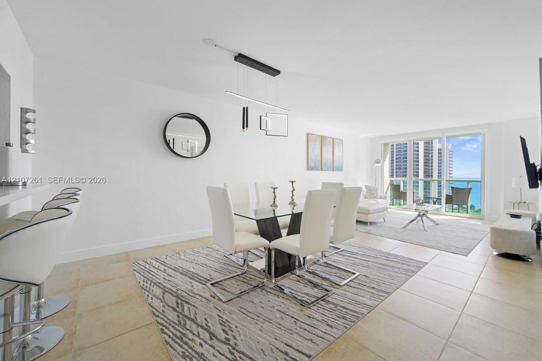 Open-concept interior featuring light-toned tile flooring, built-in breakfast bar, modern geometric pendant lighting, and floor-to-ceiling glass sliding doors