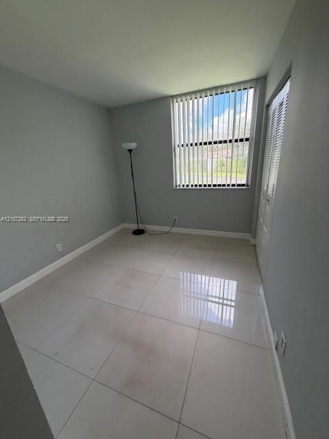 Large-format neutral tile flooring, window featuring vertical blinds, and bifold closet doors