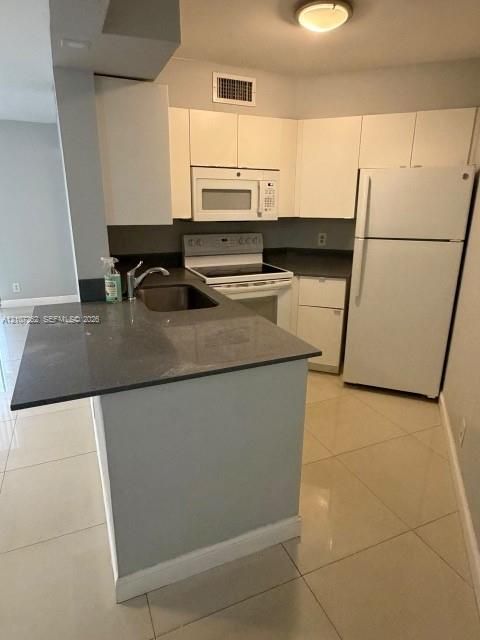 Kitchen featuring white cabinetry, solid-surface countertops, tile flooring, and integrated white appliances