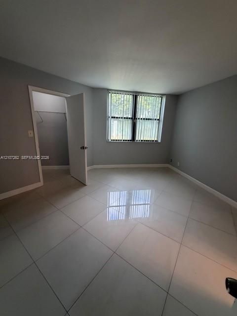 Large-format neutral tile flooring, window with vertical blinds, and interior storage space featuring a built-in rod