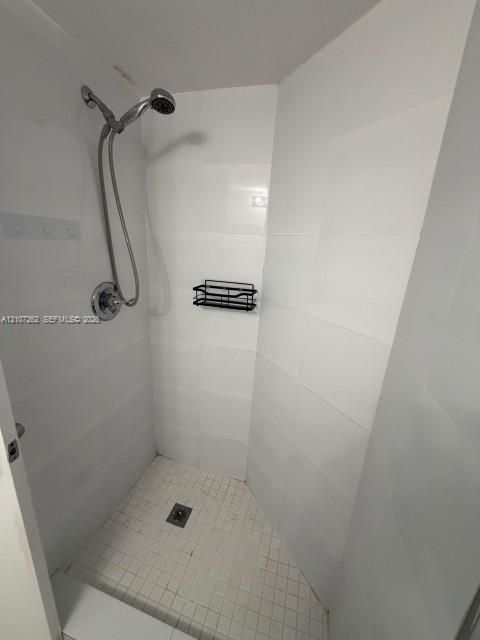 Shower enclosure featuring white wall tiling, mosaic floor tiling, a handheld shower fixture, and a built-in caddy