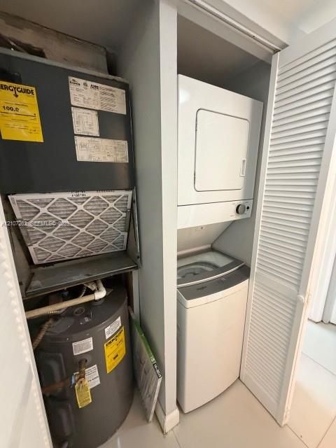 Utility closet featuring a stacked washer and dryer unit, an electric water heater, and a climate control system