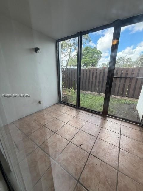 Enclosed porch featuring large floor-to-ceiling windows, ceramic tile flooring, and a wall-mounted light fixture, with access to a fenced rear yard