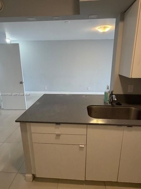 Kitchen featuring stone-finish countertops, stainless steel undermount sink, white cabinetry with horizontal hardware, and large-format tile flooring