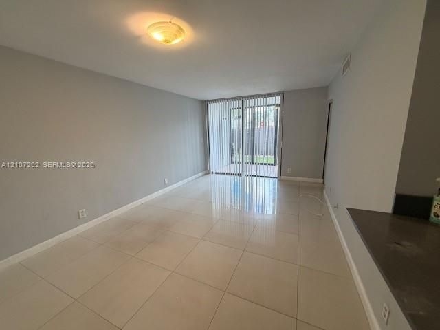 Living area featuring large-format ceramic tile flooring, neutral wall tones, flush-mount ceiling lighting, and sliding glass doors with vertical blinds