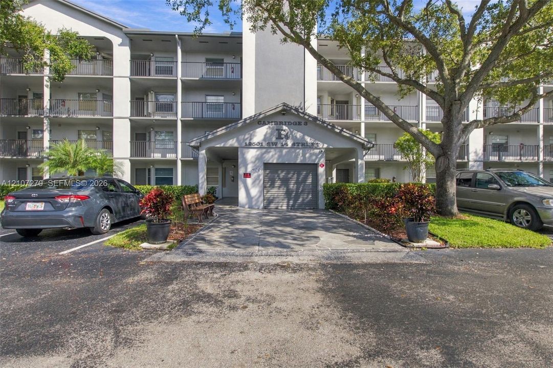 Multi-story exterior featuring a covered entryway, private garage, tiered balconies with metal railings, and mature landscaping