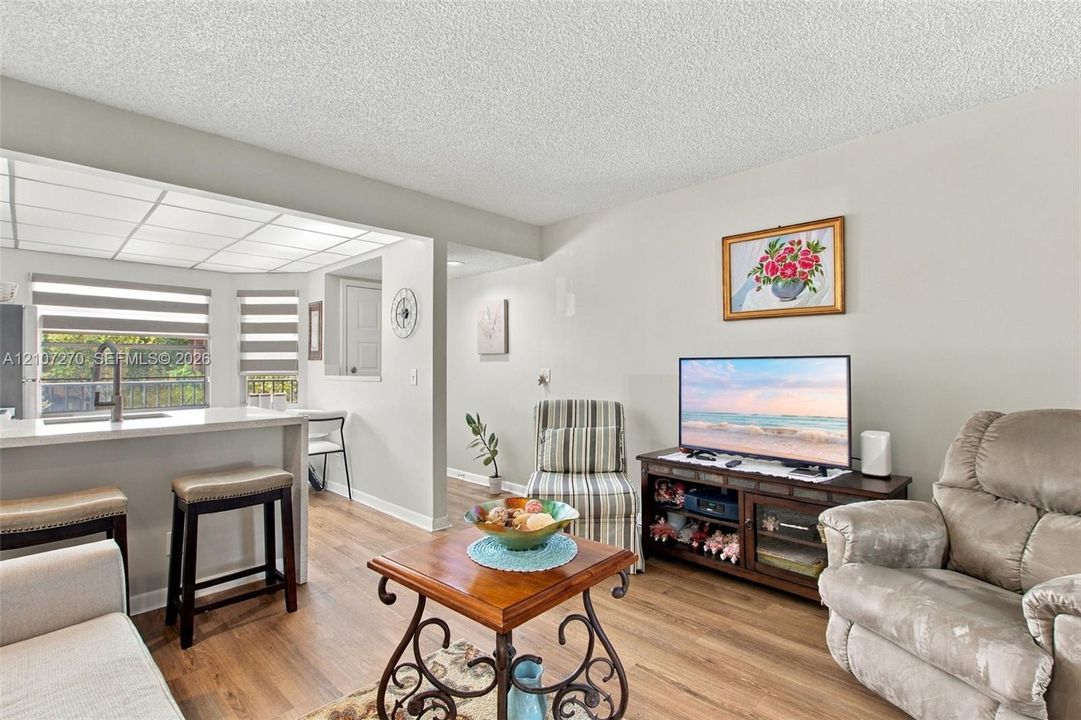 Open-concept interior featuring wood-finish flooring, a kitchen peninsula with a quartz countertop, and recessed ceiling panels with integrated lighting