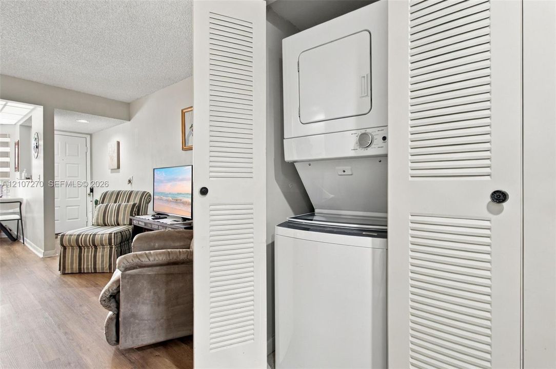 Laundry closet featuring louvered bifold doors and a stacked washer and dryer unit