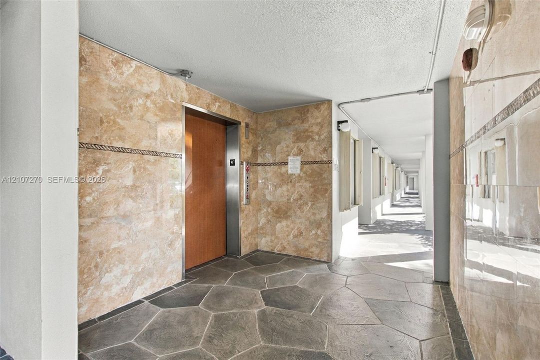 Elevator lobby featuring polished stone wall cladding, decorative tile border accents, and flagstone-style flooring